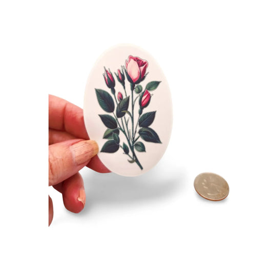 Circular sticker with floral design held by a hand next to a coin for scale on a white background