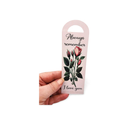 Hand holding a bookmark with floral design and text on a white background