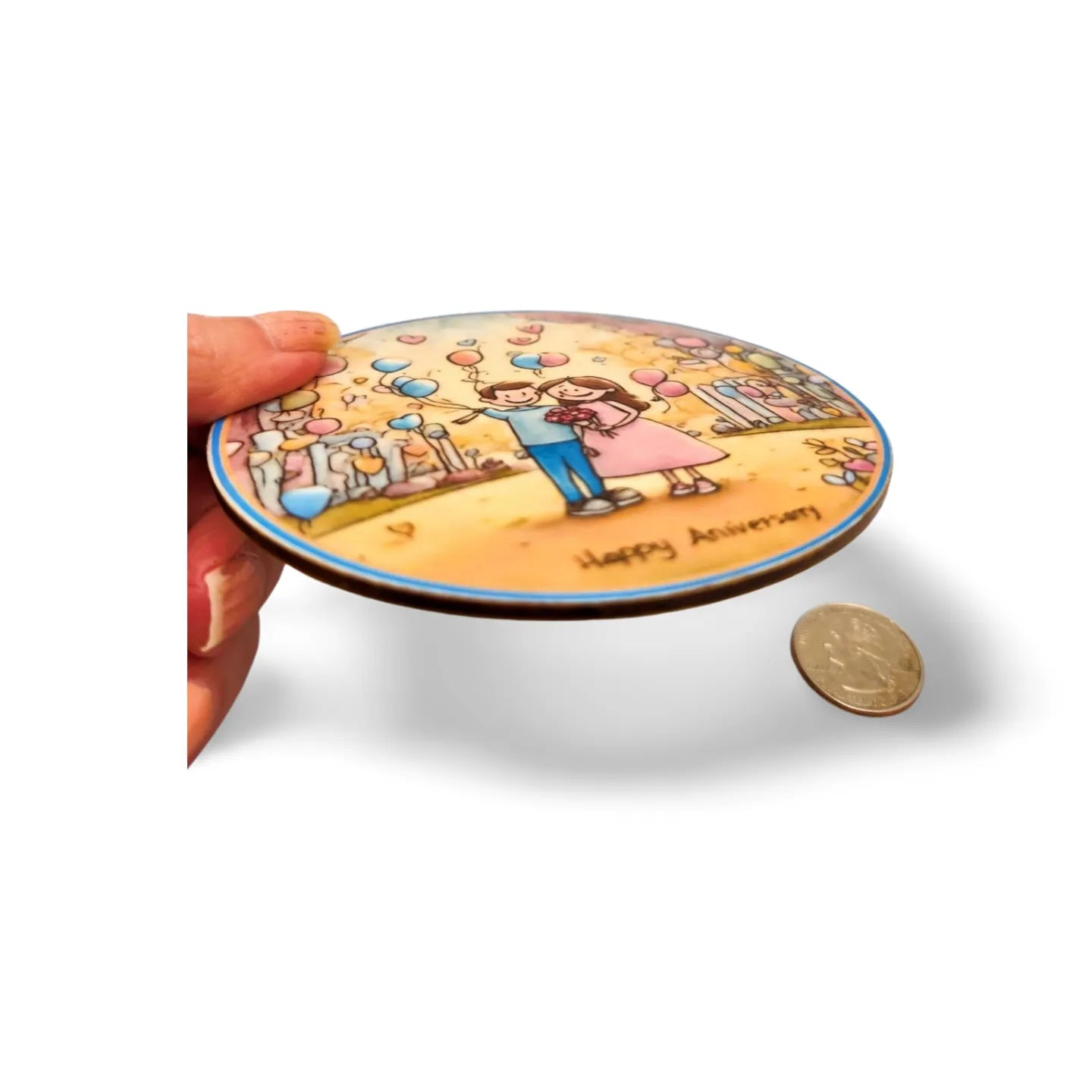 Round disc with a printed design of a couple and 'Happy Anniversary' text, held by a hand with a coin for scale.