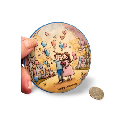Round decorative item with a couple and balloons illustration, held by a hand.