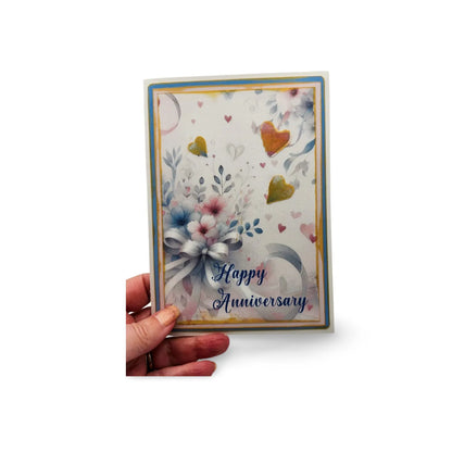 Hand holding a 'Happy Anniversary' card with floral design on a white background