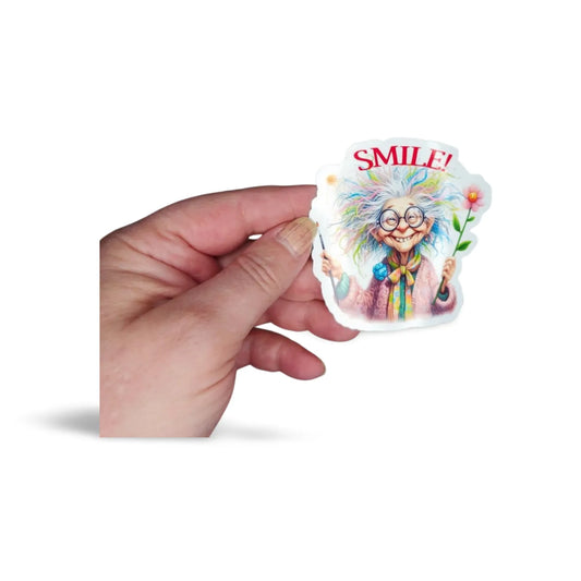 Hand holding a colorful sticker with a cartoon character and 'SMILE!' text on a white background