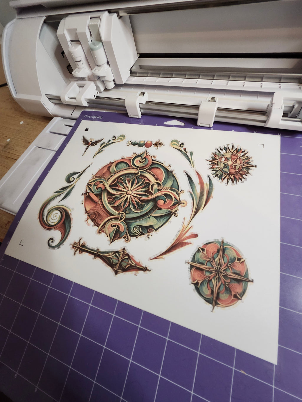 Cricut machine with decorative paper featuring intricate designs on a purple grid background