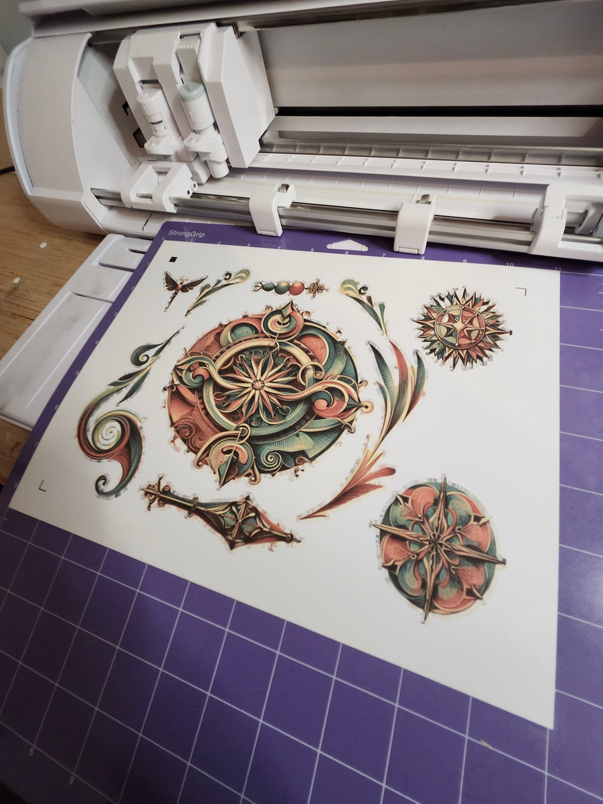Cricut machine with decorative paper featuring intricate designs on a purple grid background