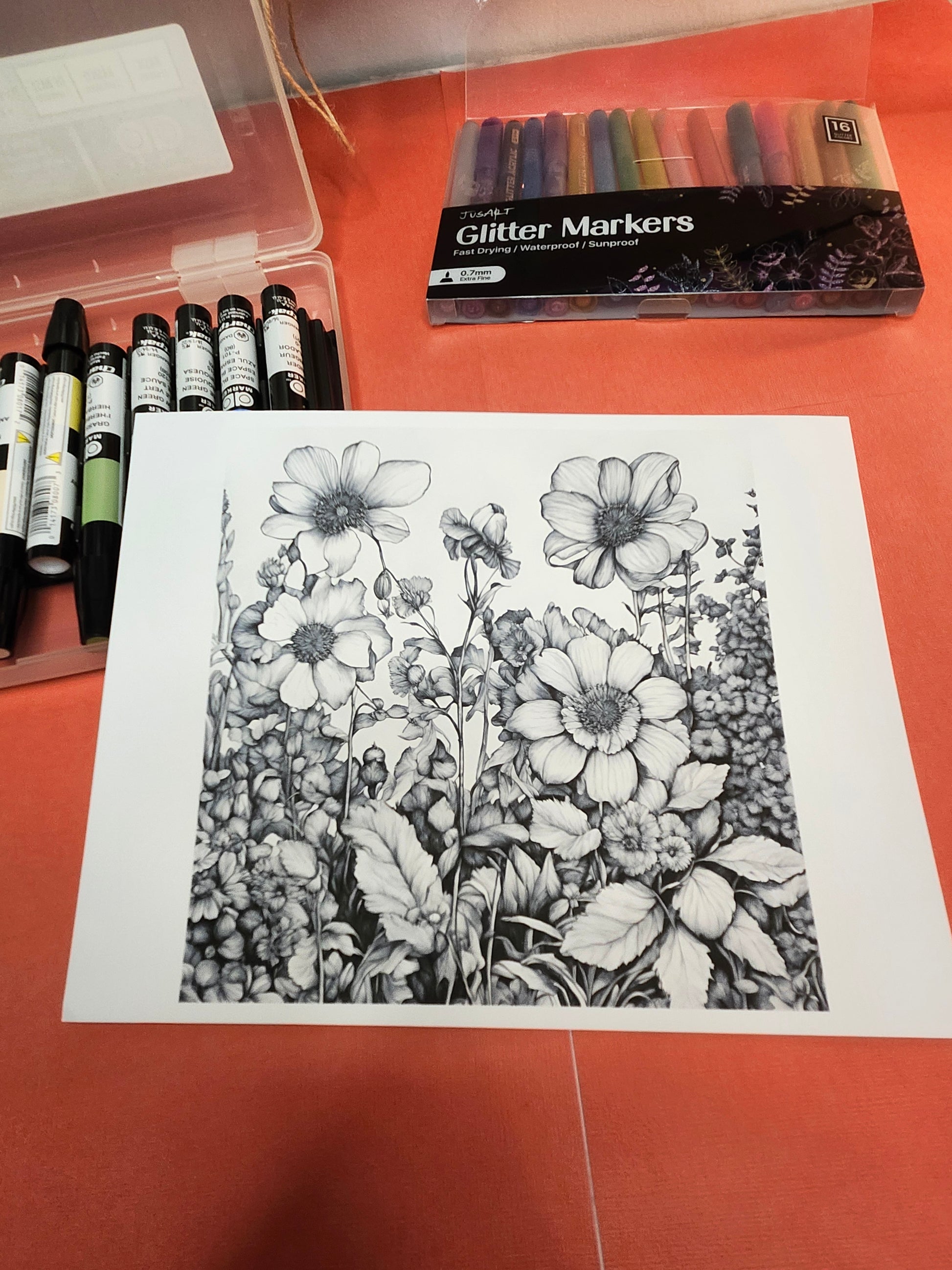 Floral drawing on paper with glitter markers and colored pencils on a red surface