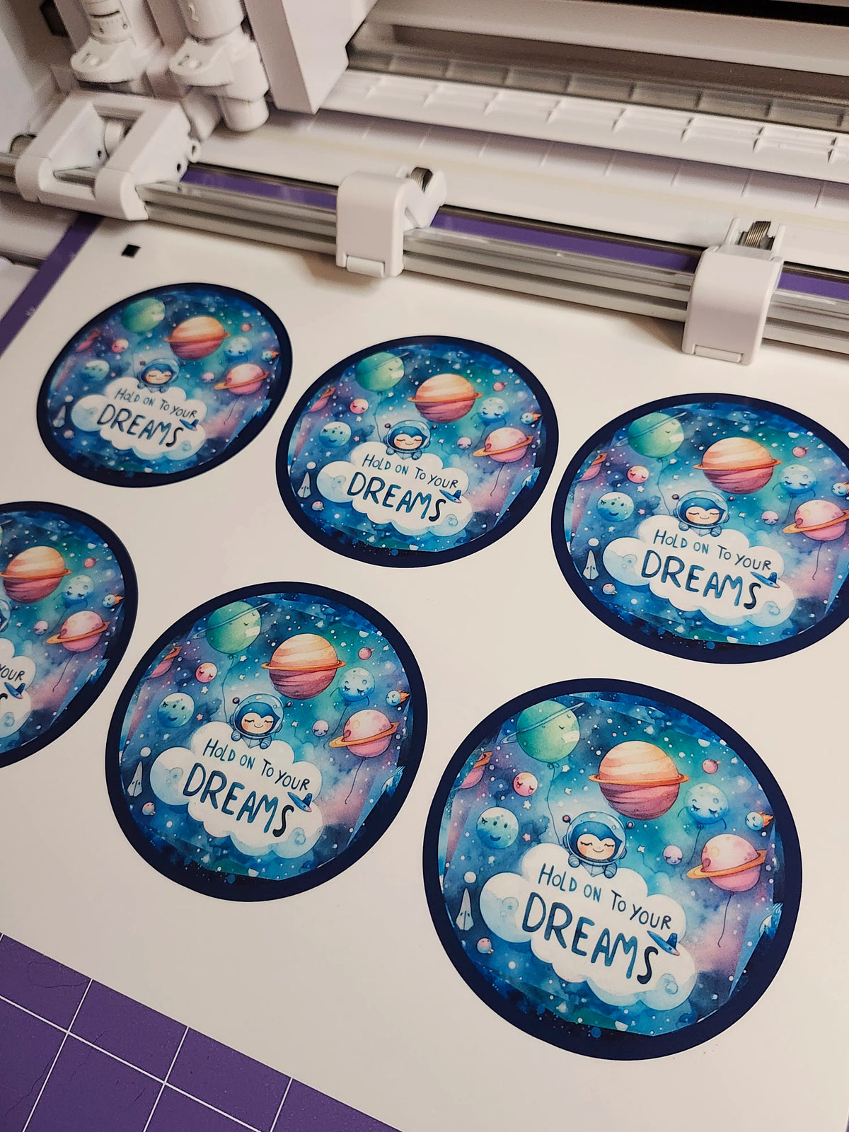 Circular stickers with space-themed designs and text on a cutting mat.