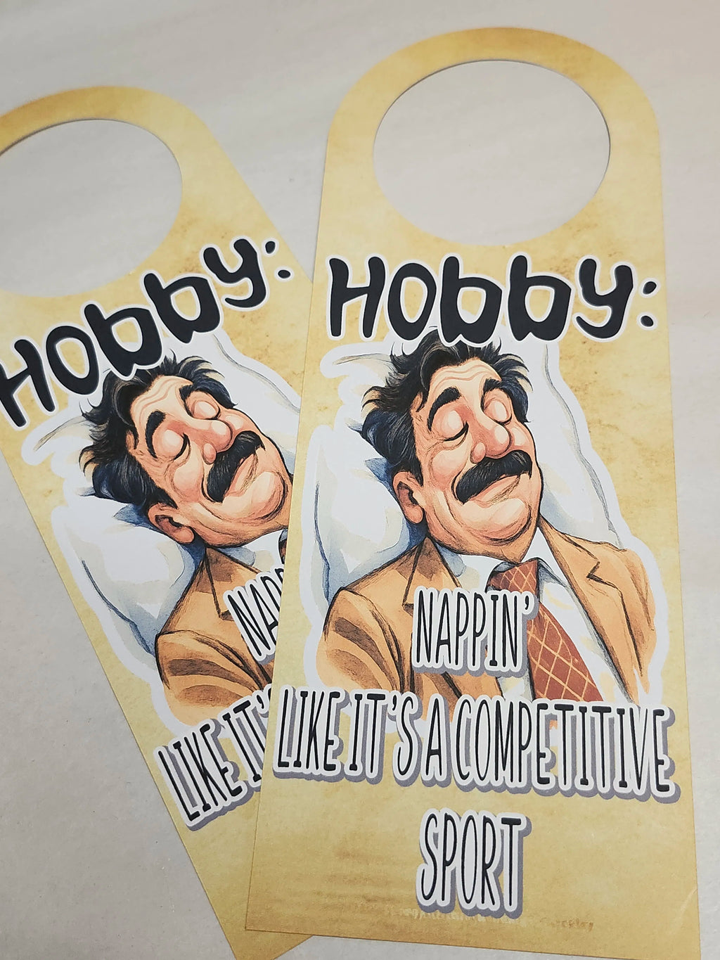 Two door hangers with a cartoon character and humorous text on a beige background.