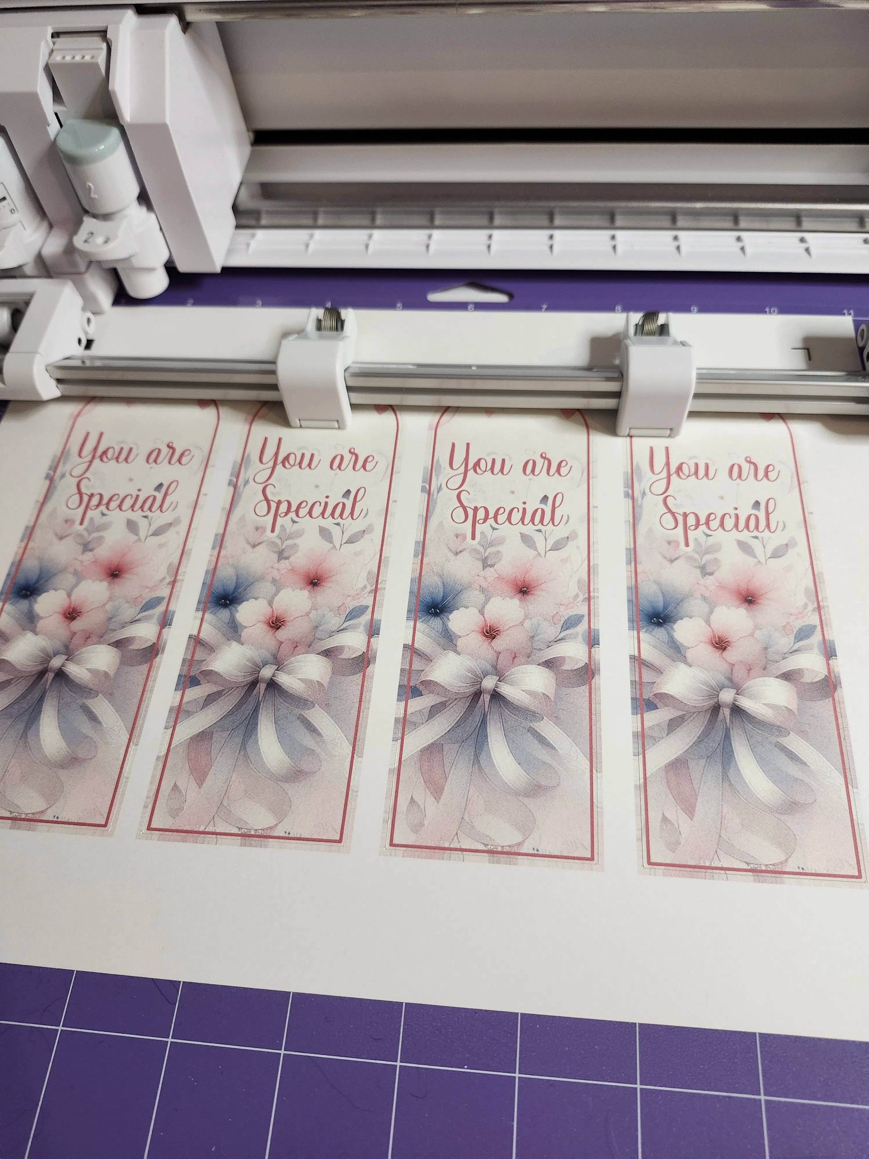 Four printed bookmarks with floral designs and 'You are Special' text on a cutting machine.