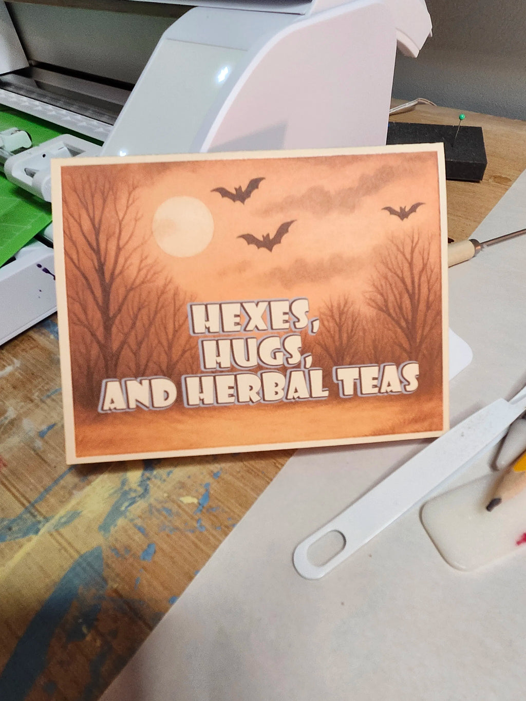 Card with Halloween-themed design featuring bats, a moon, and text on a wooden surface.