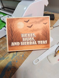 Card with Halloween-themed design featuring bats, a moon, and text on a wooden surface.