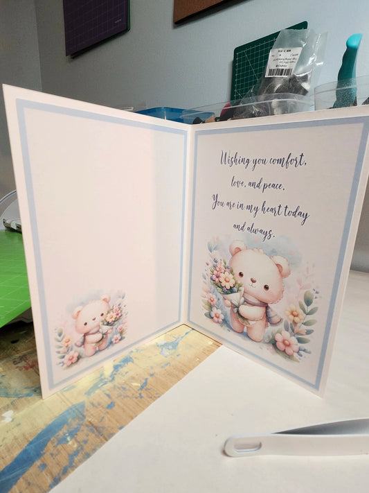 Greeting card with teddy bear illustration and heartfelt message on a desk.