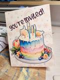 Invitation card with a colorful cake illustration and 'You're Invited!' text.