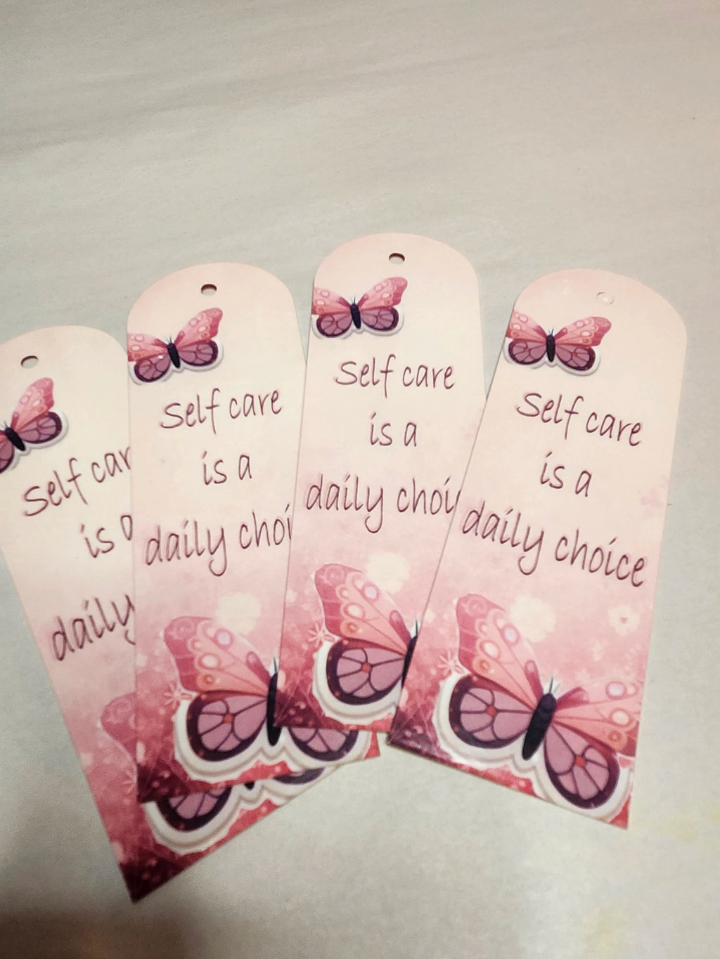 Pink bookmarks with butterfly designs and 'Self care is a daily choice' text on a light background
