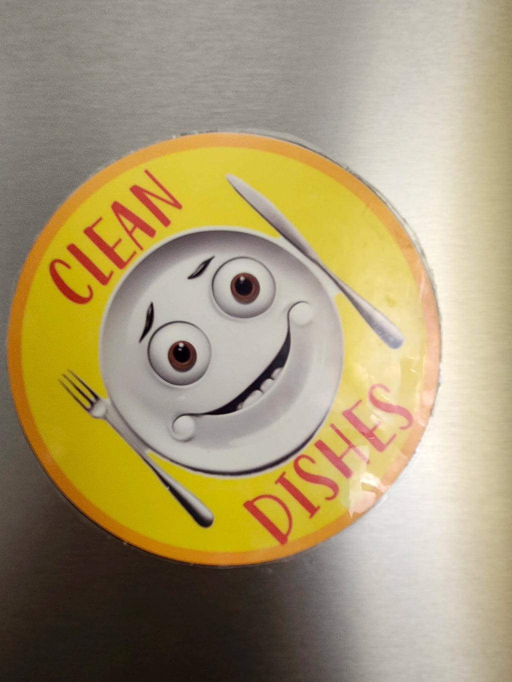 Circular magnet with cartoon character and 'Clean Dishes' text on a metallic surface
