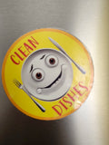 Circular magnet with cartoon character and 'Clean Dishes' text on a metallic surface