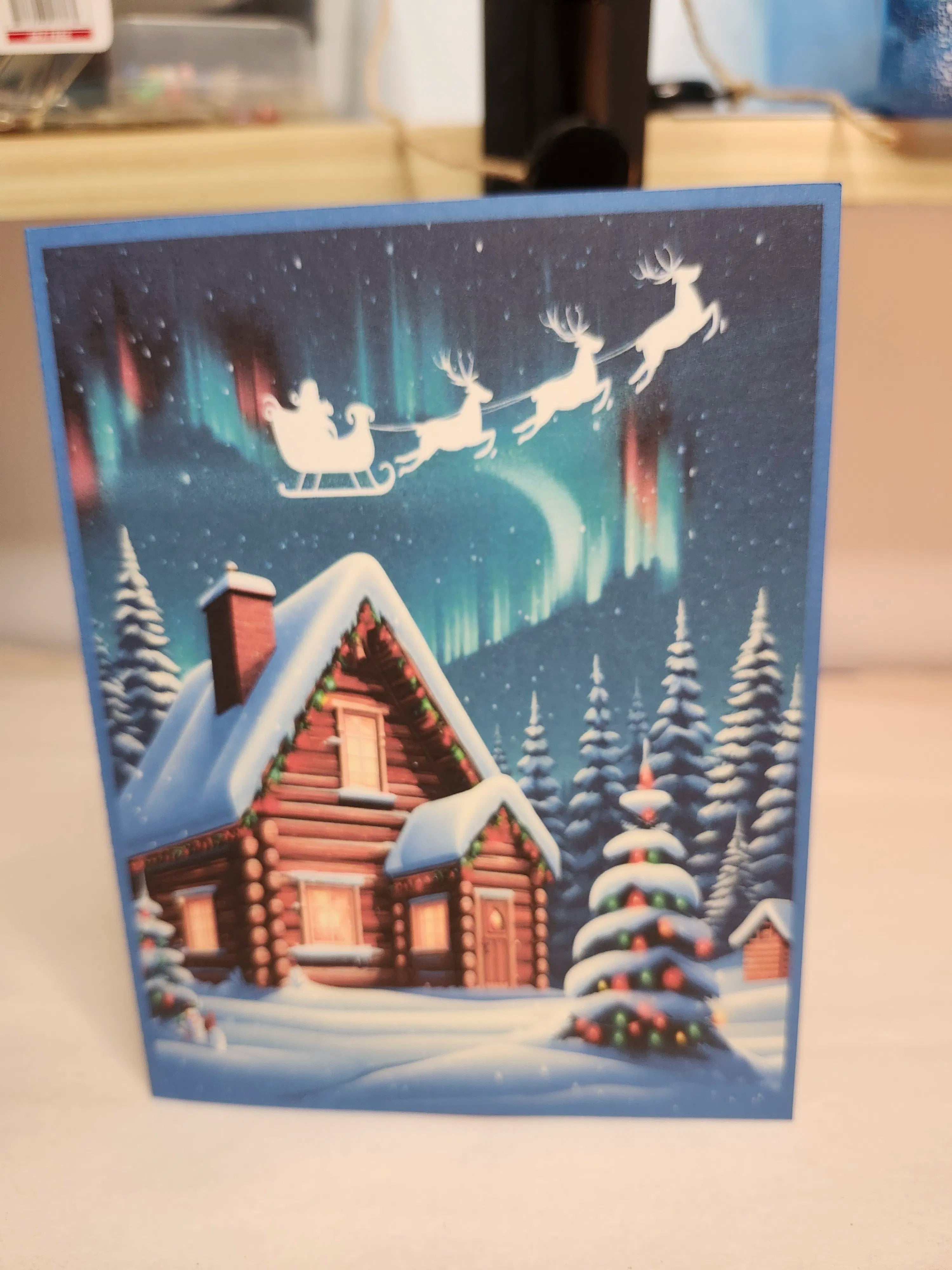 Christmas card with Santa Claus in a sleigh, reindeer, and a snowy cabin.