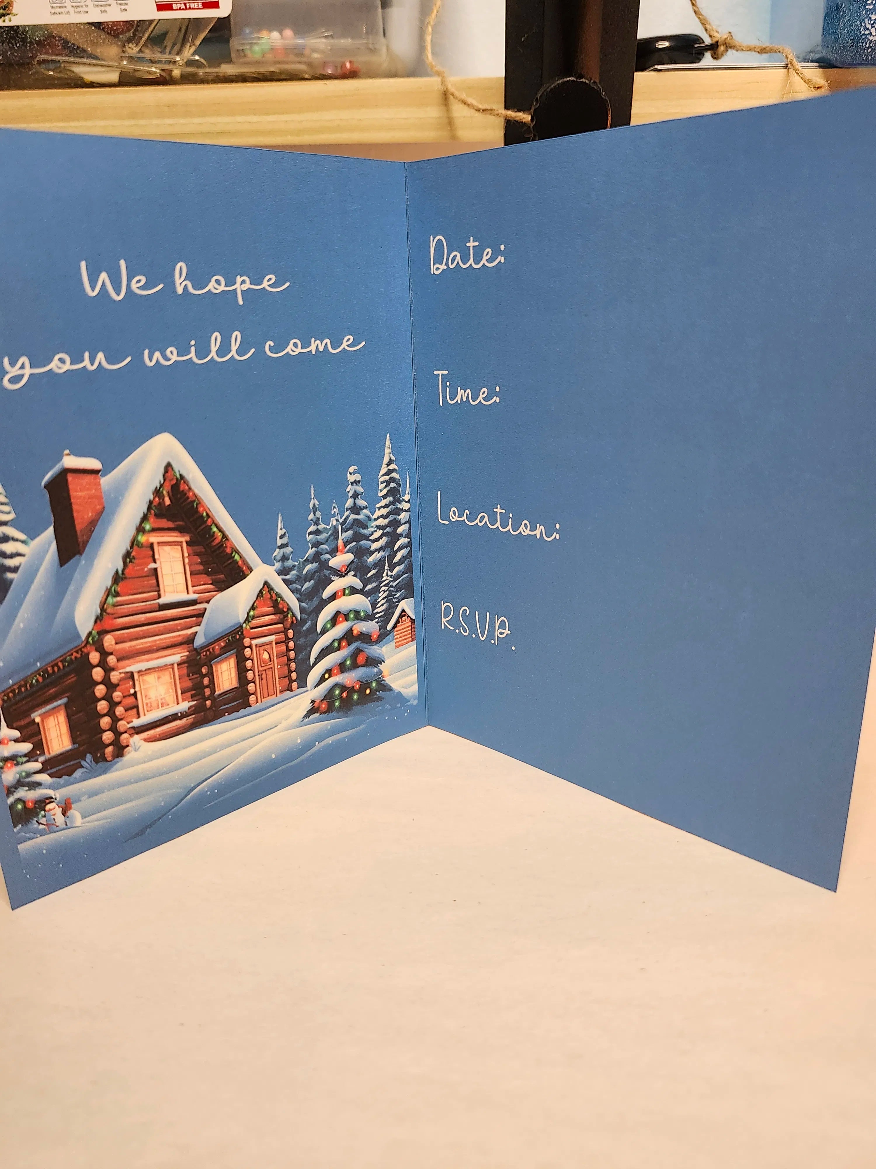 Invitation card with a snowy cabin illustration and text fields on a blue background.