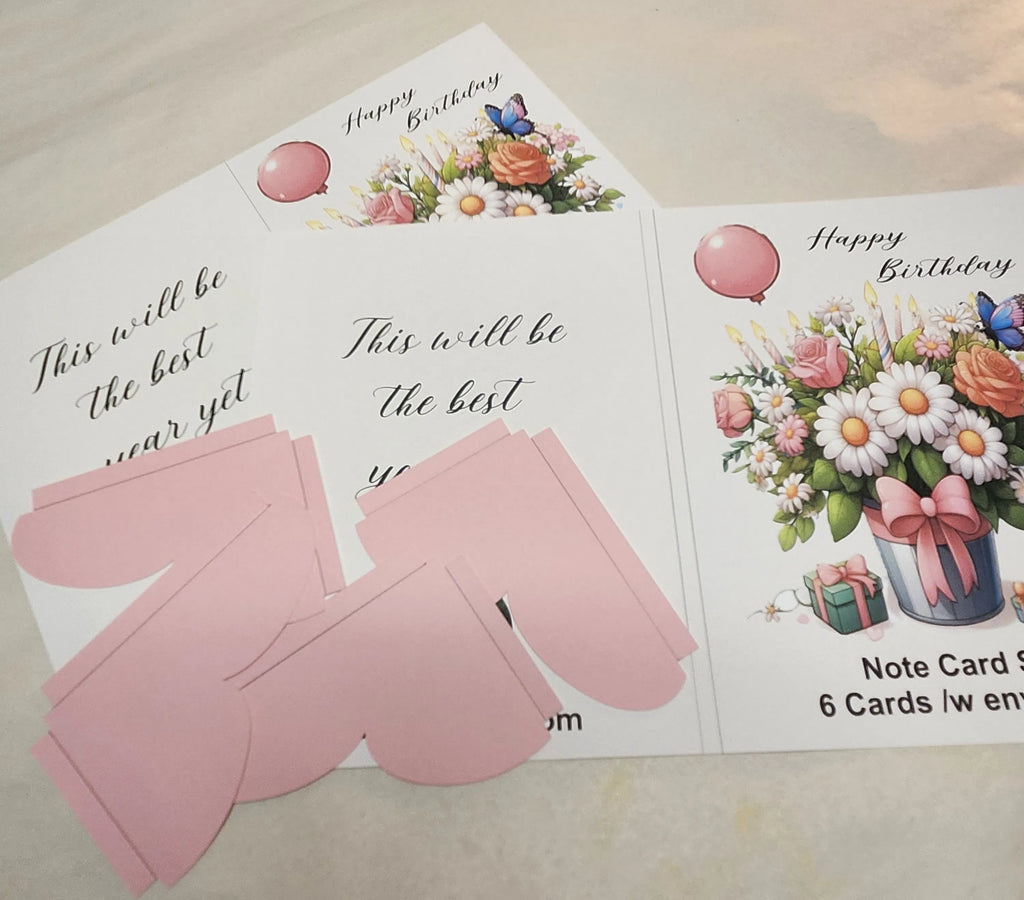 Set of birthday cards with floral designs and pink envelopes on a light surface.