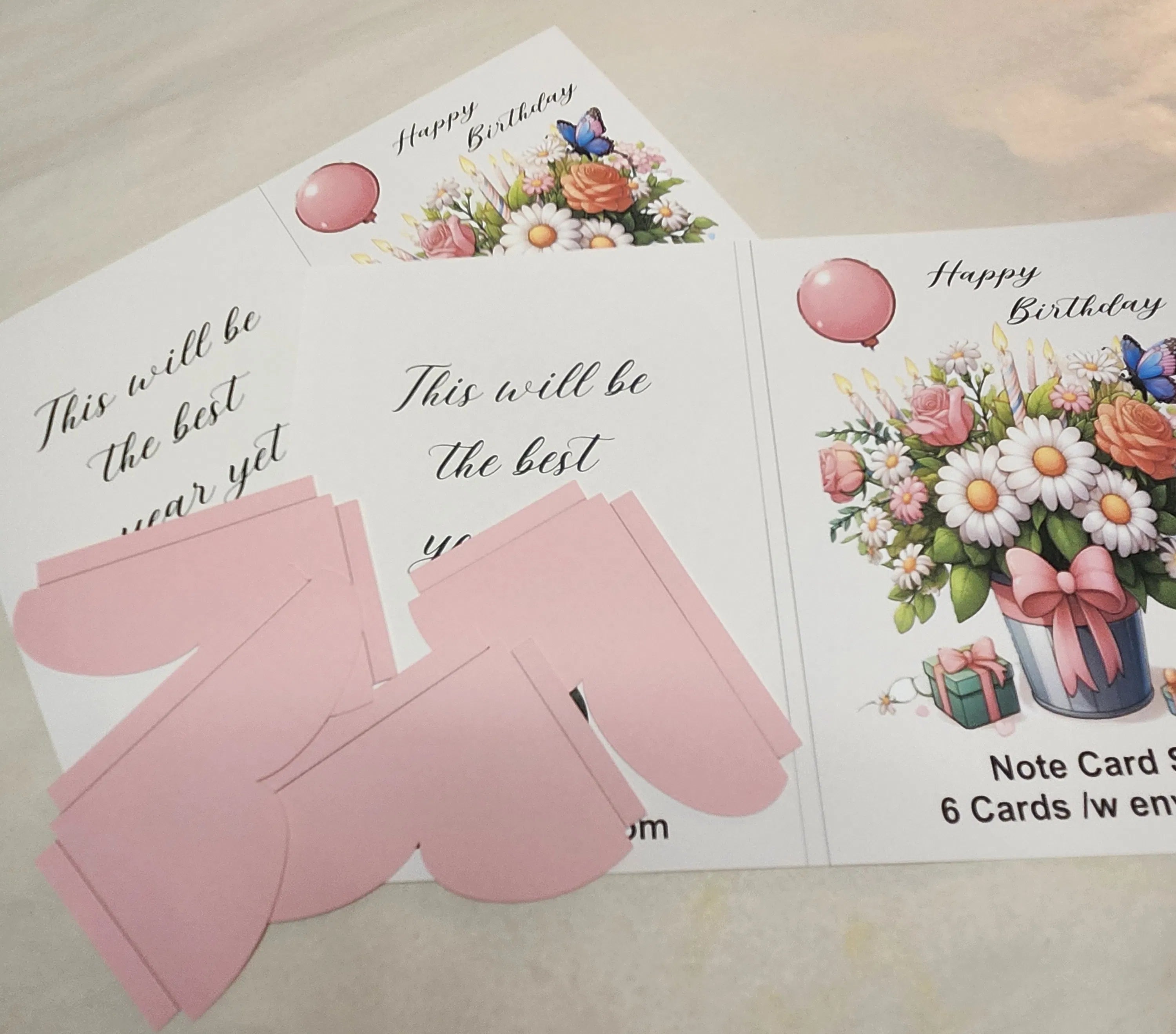 Set of birthday cards with floral designs and pink envelopes on a light surface.