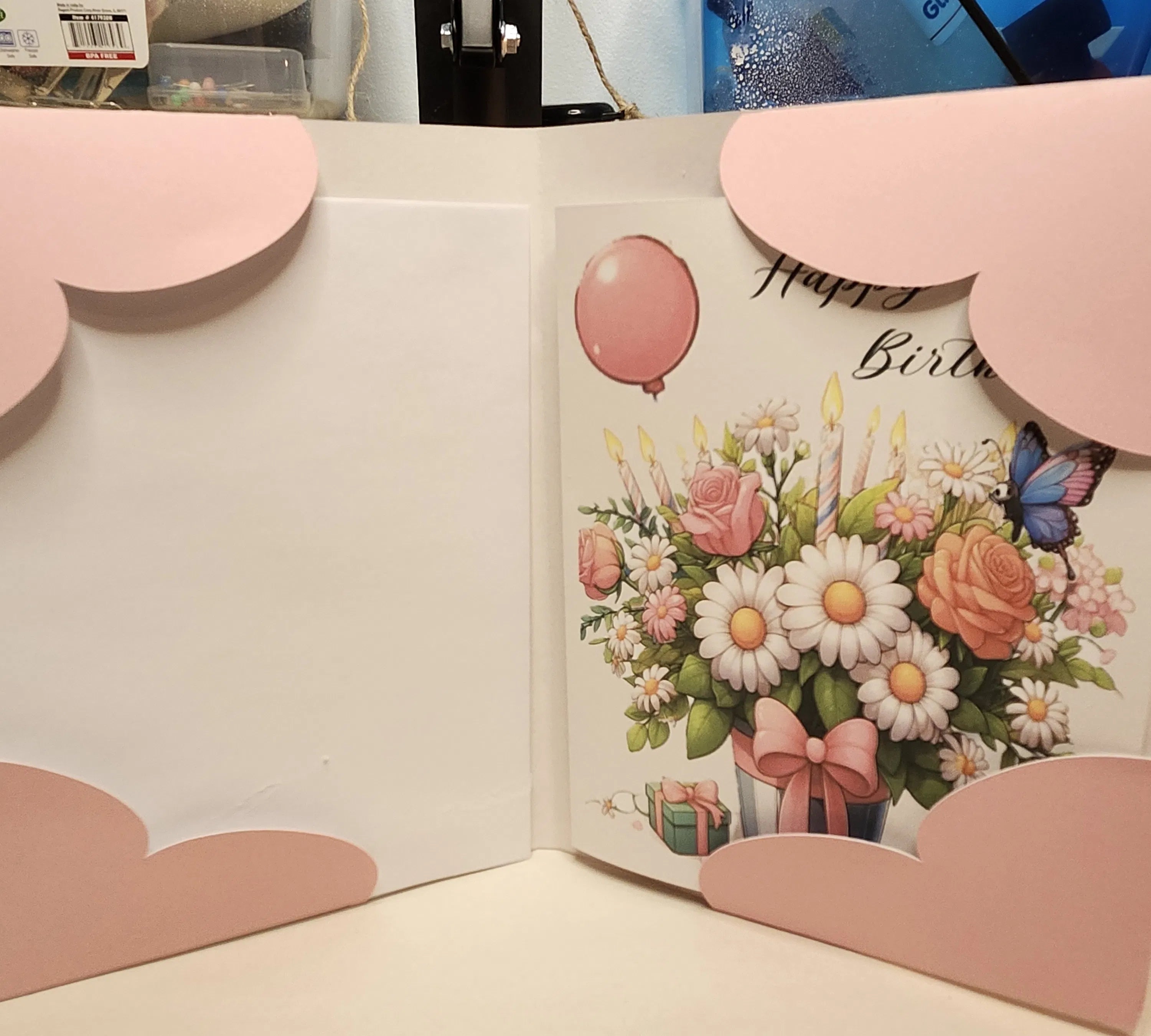 Open birthday card with floral design and pink balloons on a light background