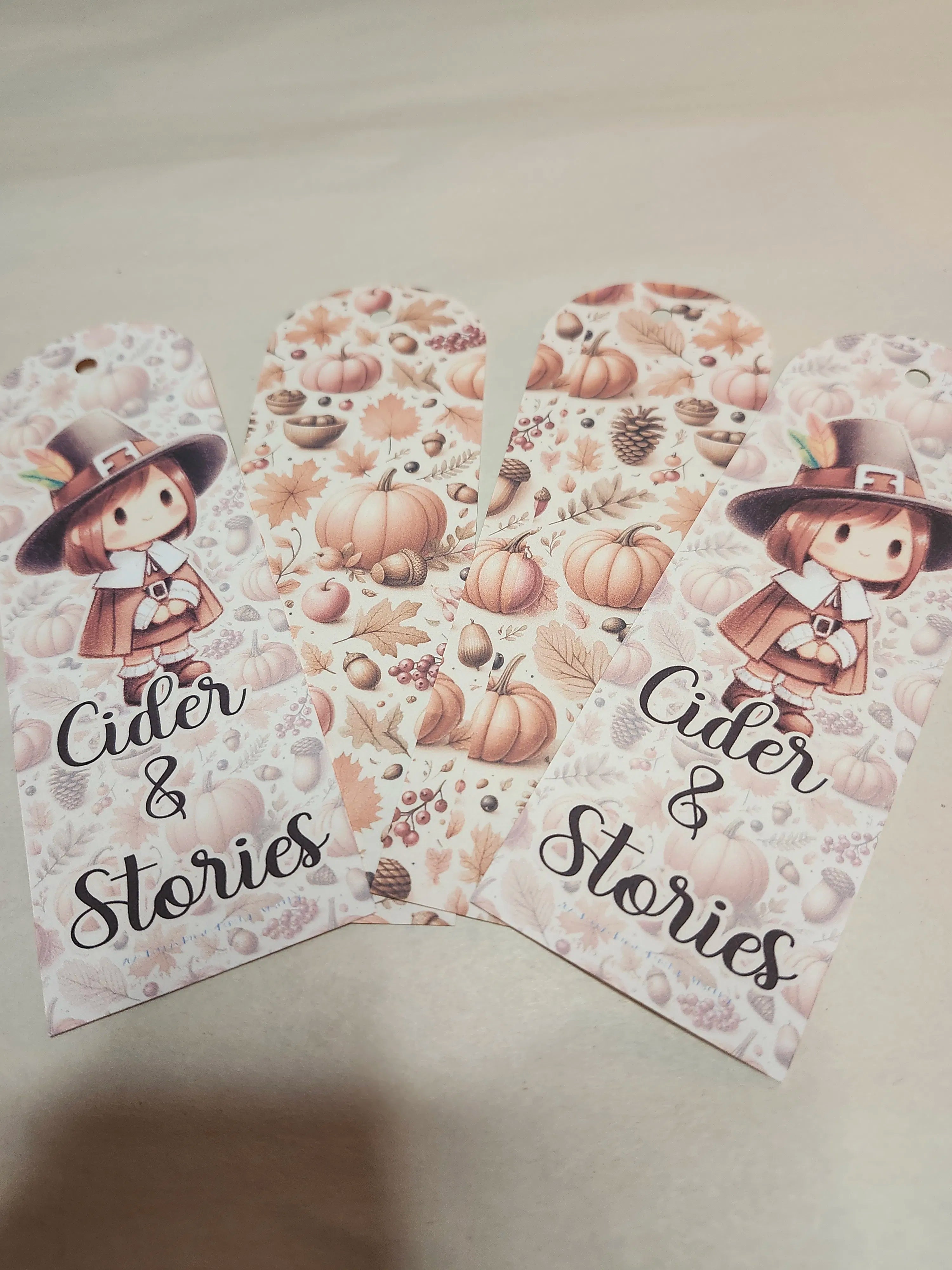 Two 'Cider & Stories' themed gift tags with a cartoon pilgrim and autumn elements on a beige background.