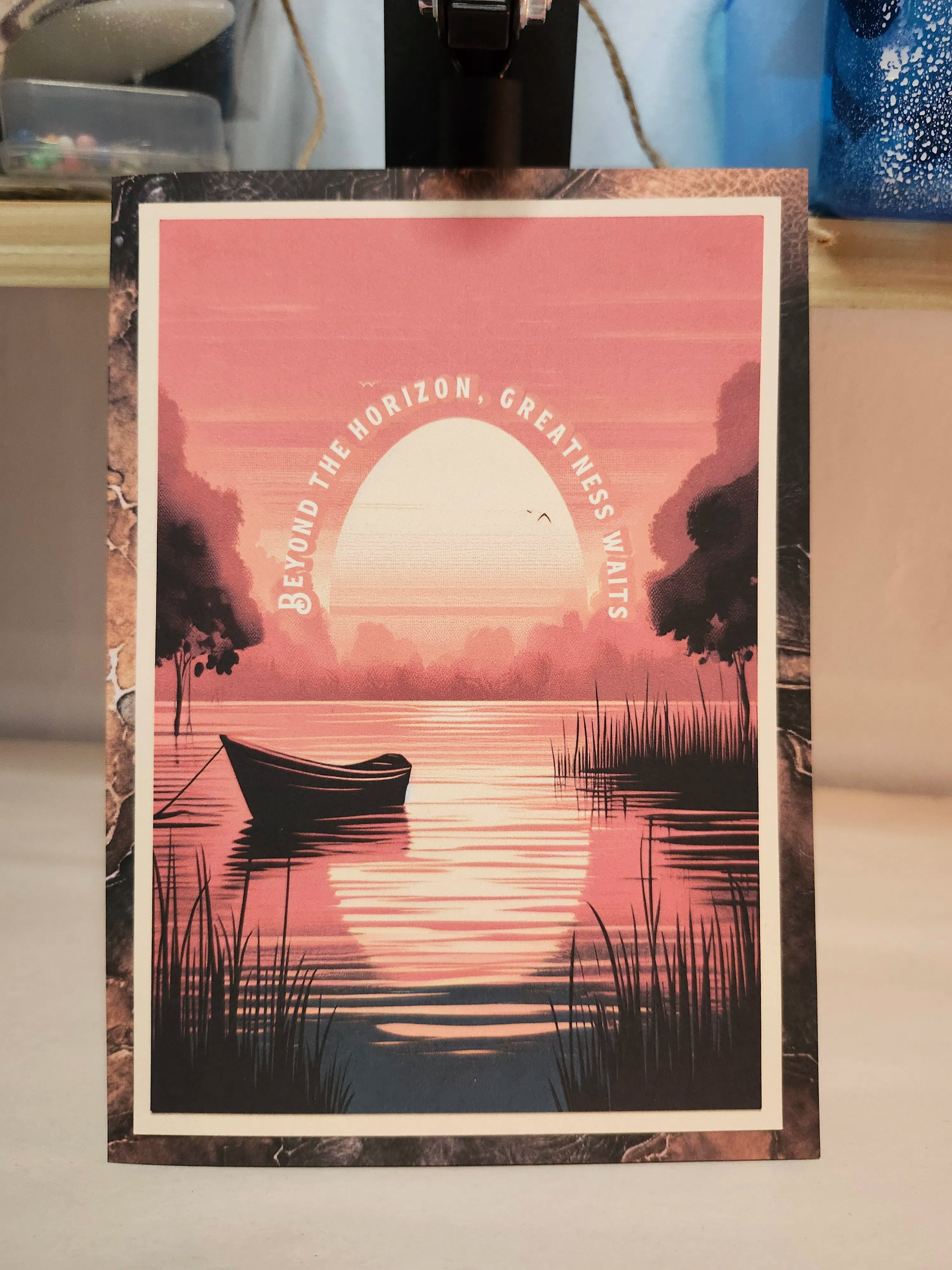 Framed poster with a sunset over a lake and a boat, with text 'Beyond the horizon, greatness waits'.