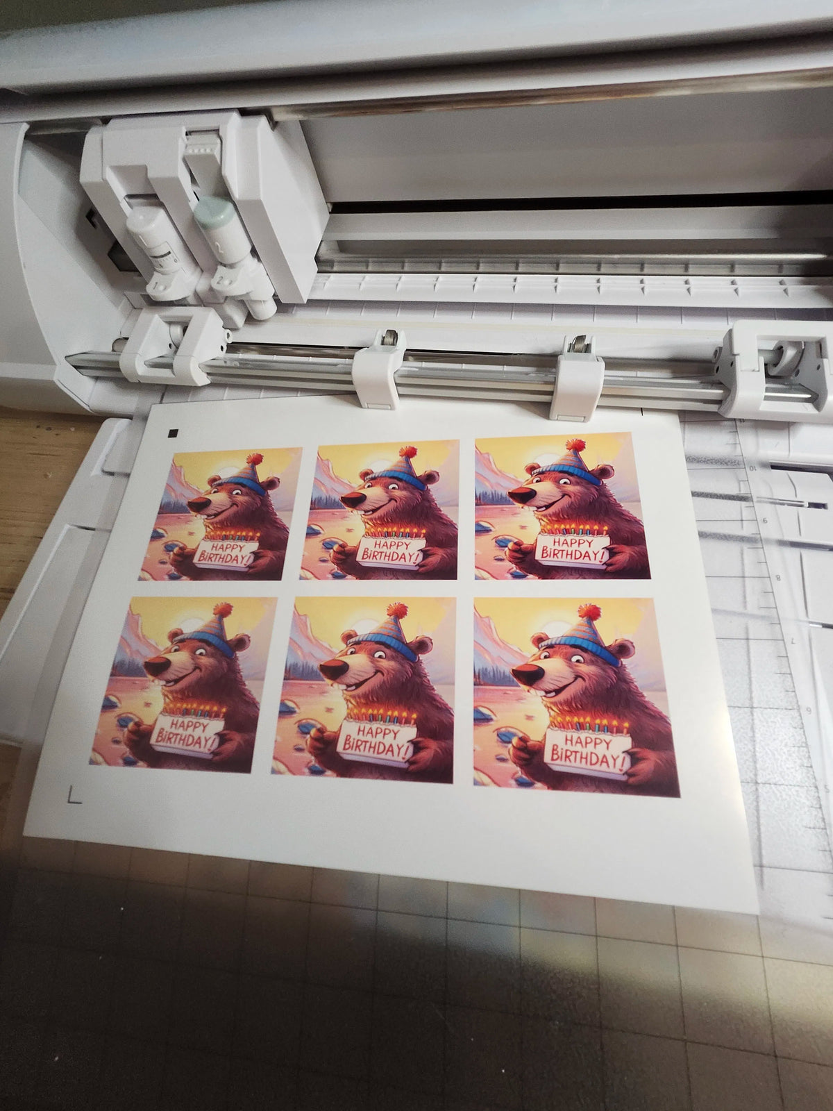 Sheet of printed birthday cards with a bear design on a printer bed.