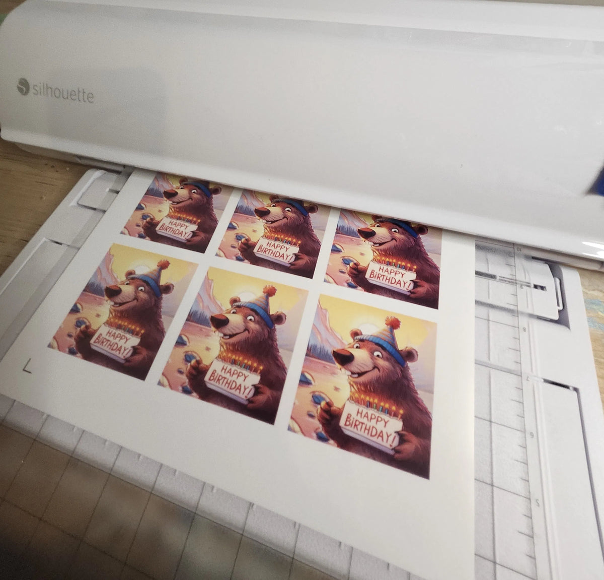 Silhouette cutting machine with printed birthday cards featuring a bear design.