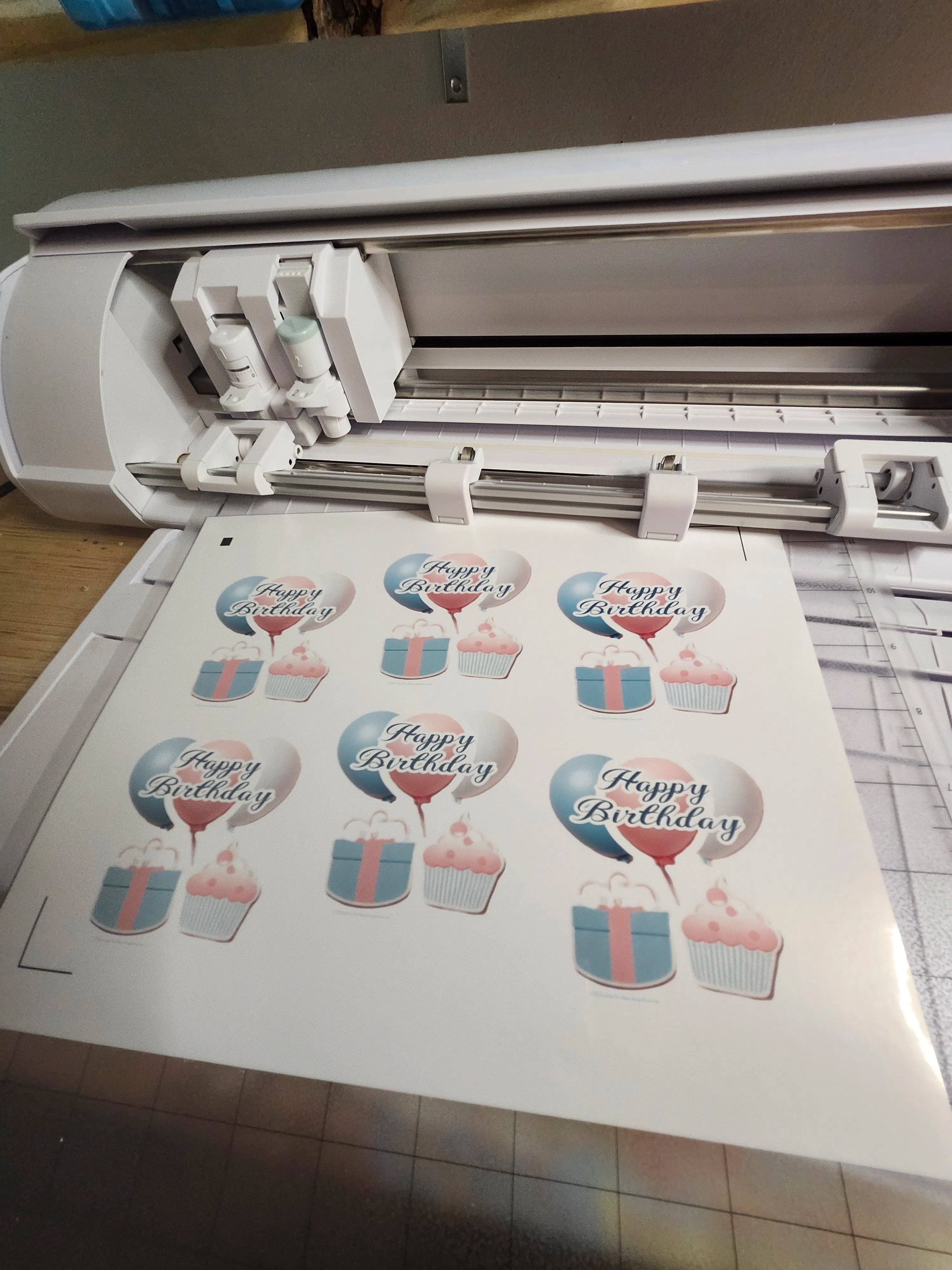 Cricut machine with printed sheet of birthday-themed cutouts on a table.