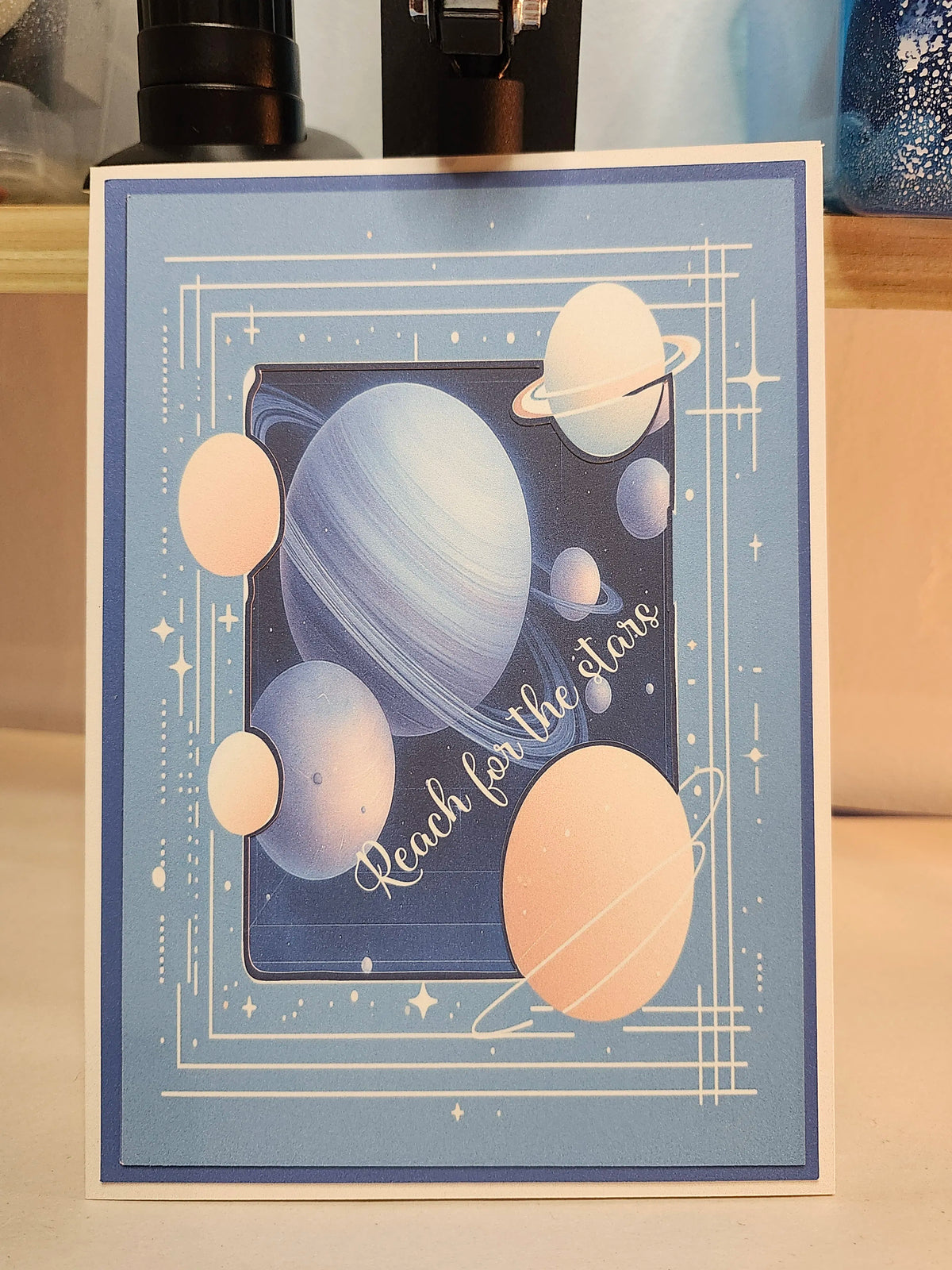 Card with space-themed design featuring planets and 'Reach for the stars' text on a blue background.