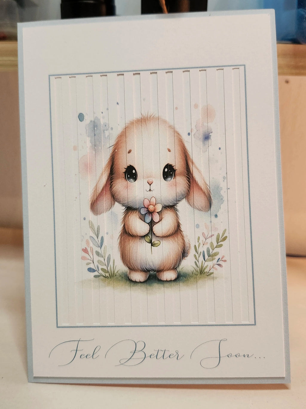 Greeting card with a bunny illustration and 'Feel Better Soon' text on a wooden surface.