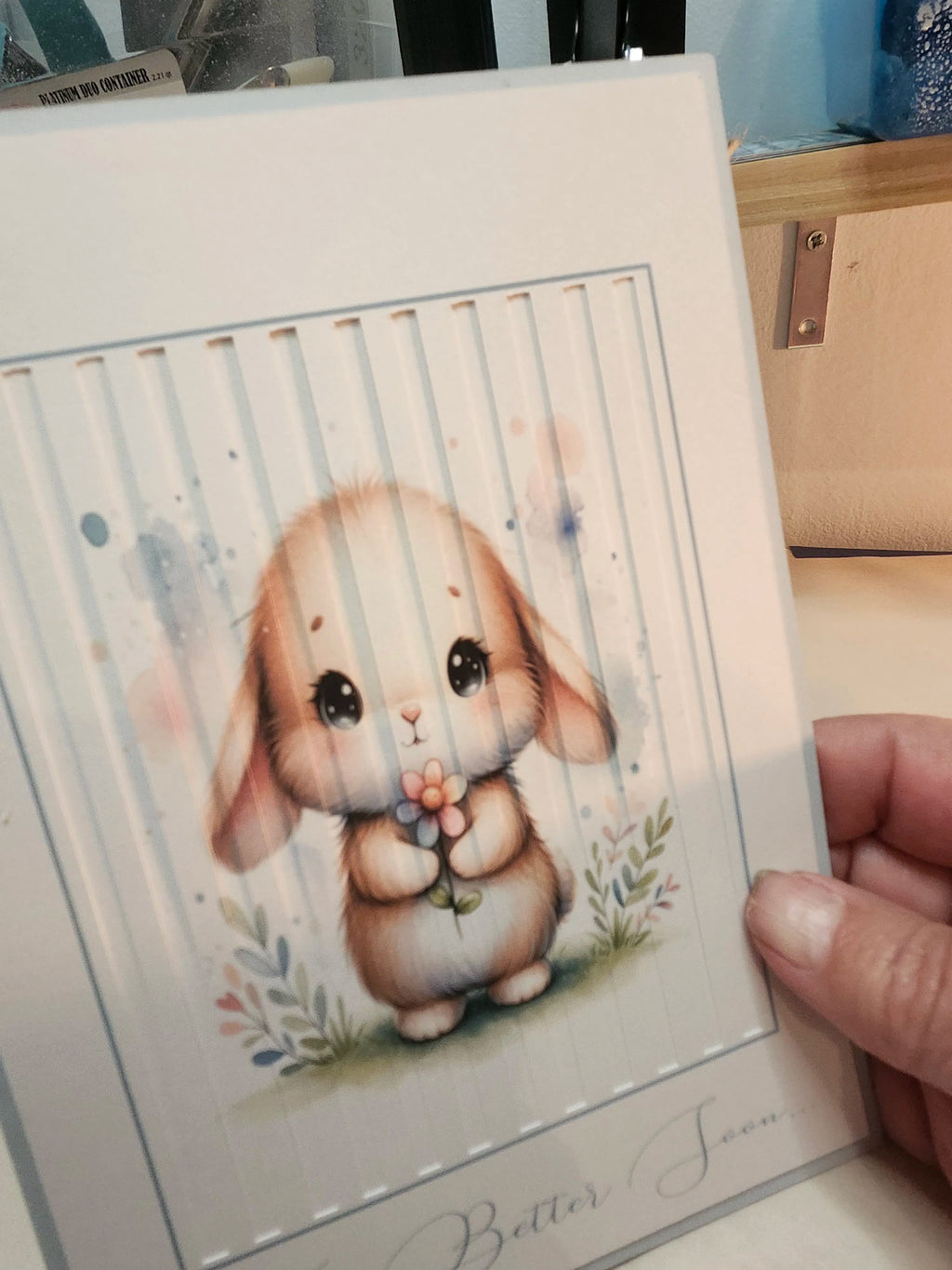 Illustration of a cute bunny holding a flower on a card held by a hand.