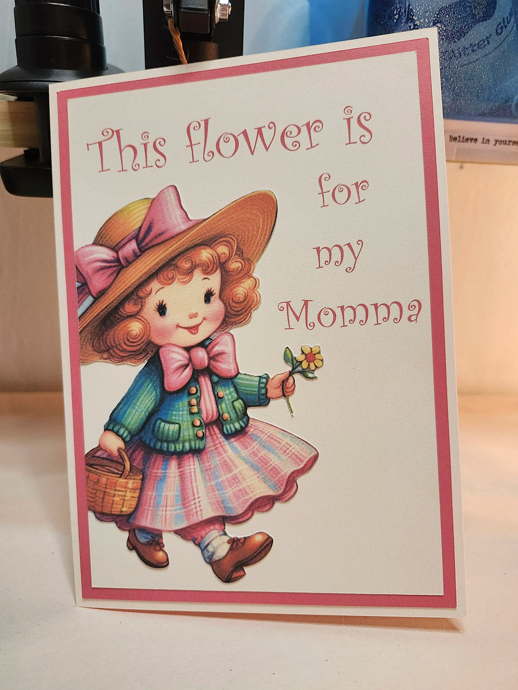 Card with a vintage-style illustration of a girl holding a flower, with text 'This flower is for my Momma'.