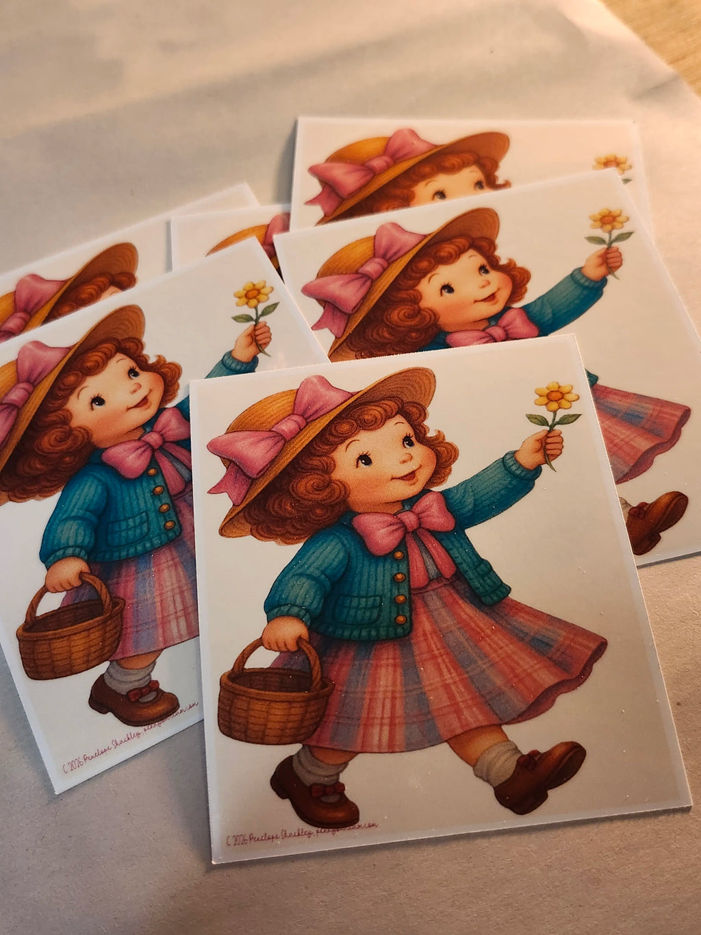 Set of illustrated stickers featuring a girl with a basket and flower, on a light surface.