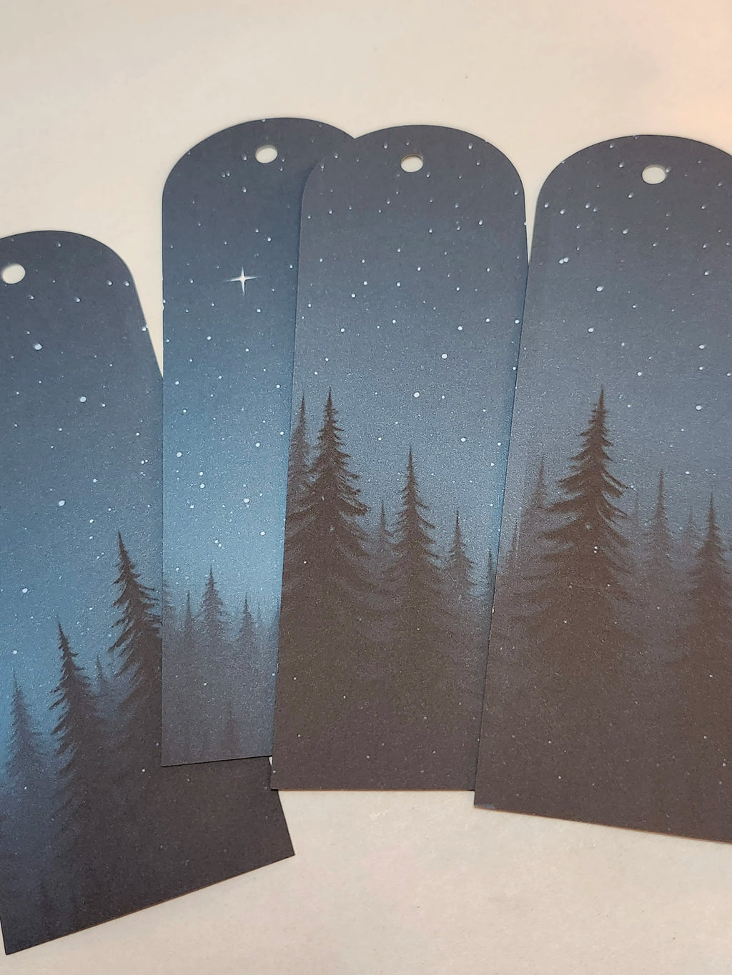 Four bookmarks with a design of trees and stars on a gradient blue background.