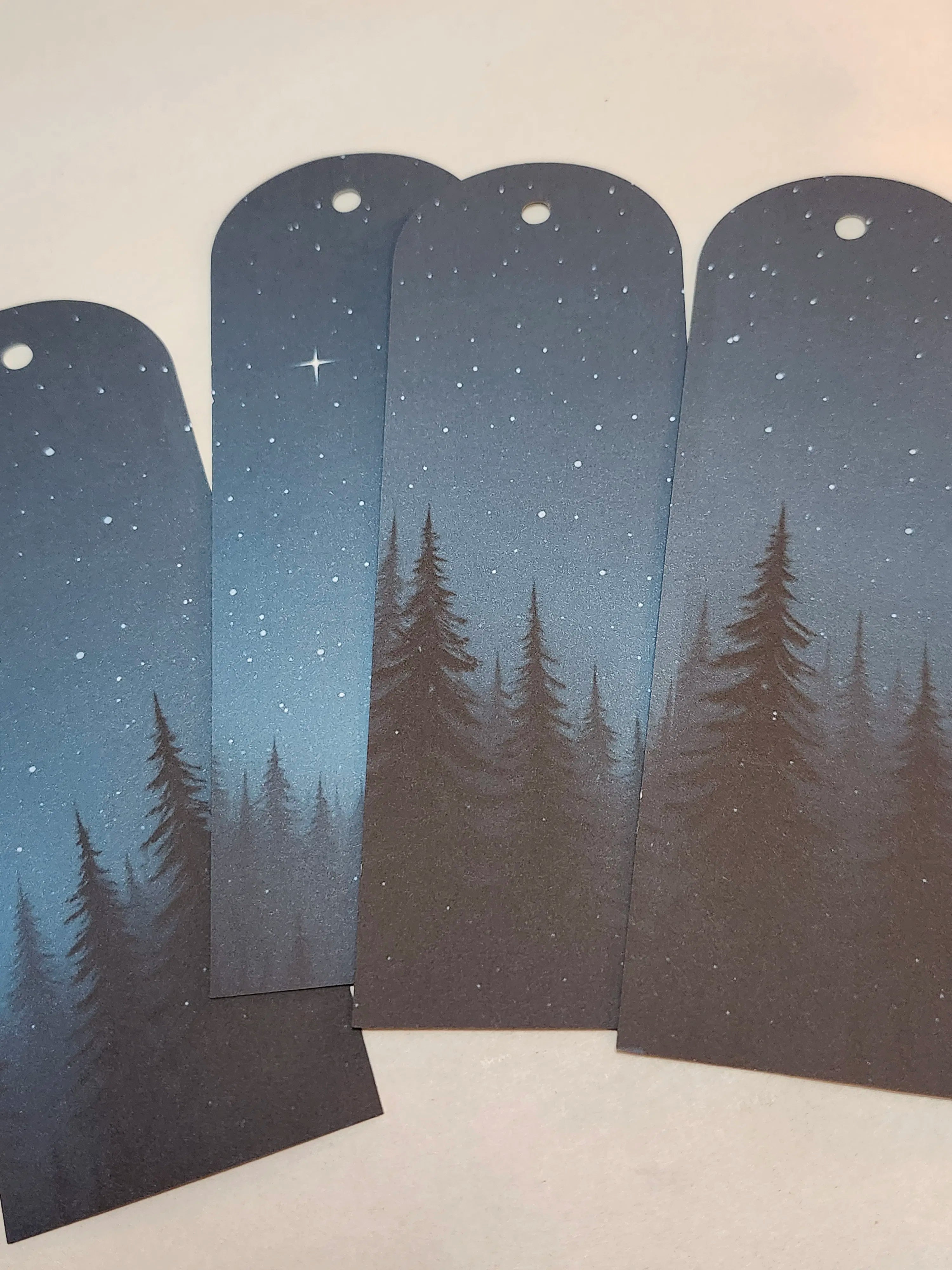 Four bookmarks with a design of trees and stars on a gradient blue background.
