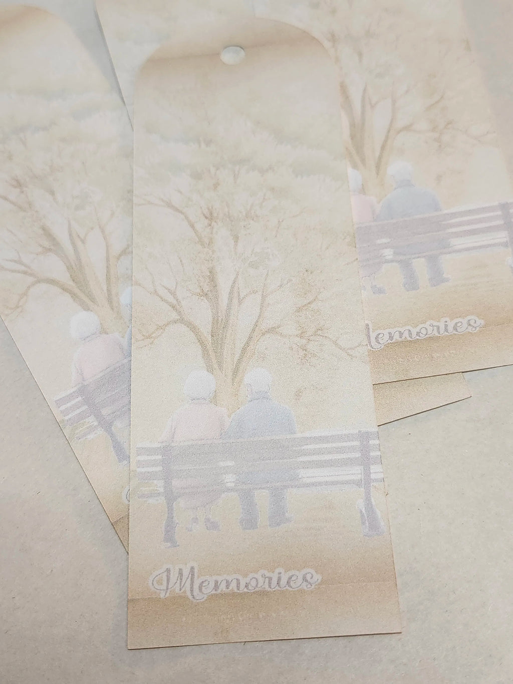 Bookmarks with a printed design of people on a bench under trees, with 'Memories' text.