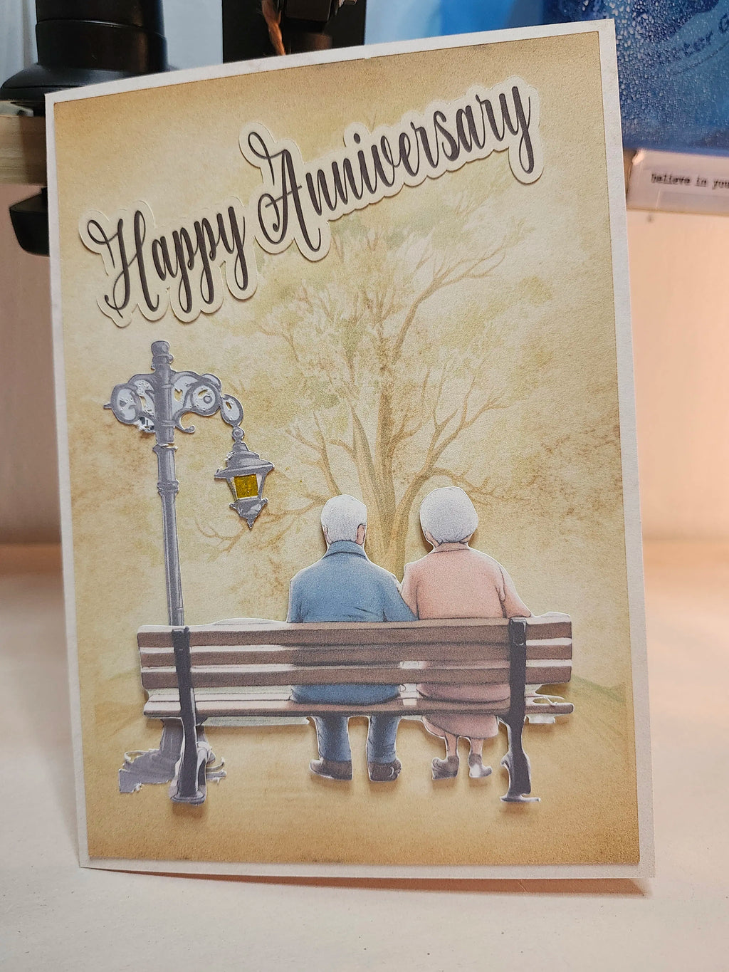 Anniversary card with an illustration of an elderly couple on a bench under a tree.