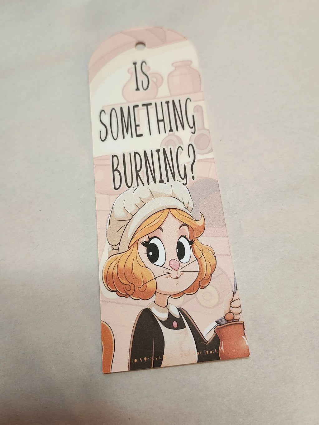 Cartoon character with a chef hat and apron, holding a spatula, with text 'Is something burning?' on a beige background.