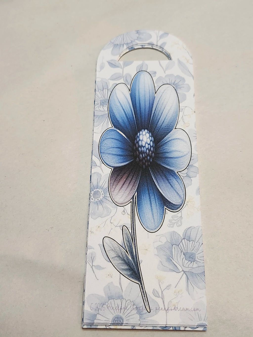Decorative bookmark with a blue flower design on a beige background