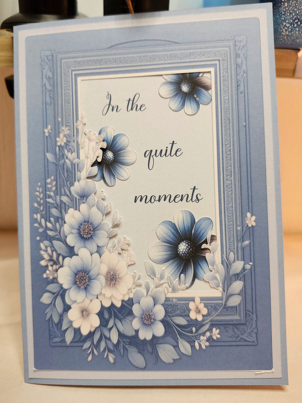 Greeting card with floral design and text 'In the quite moments' on a wooden surface.