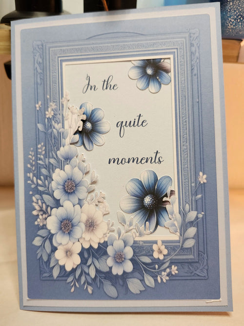 Greeting card with floral design and text 'In the quite moments' on a wooden surface.
