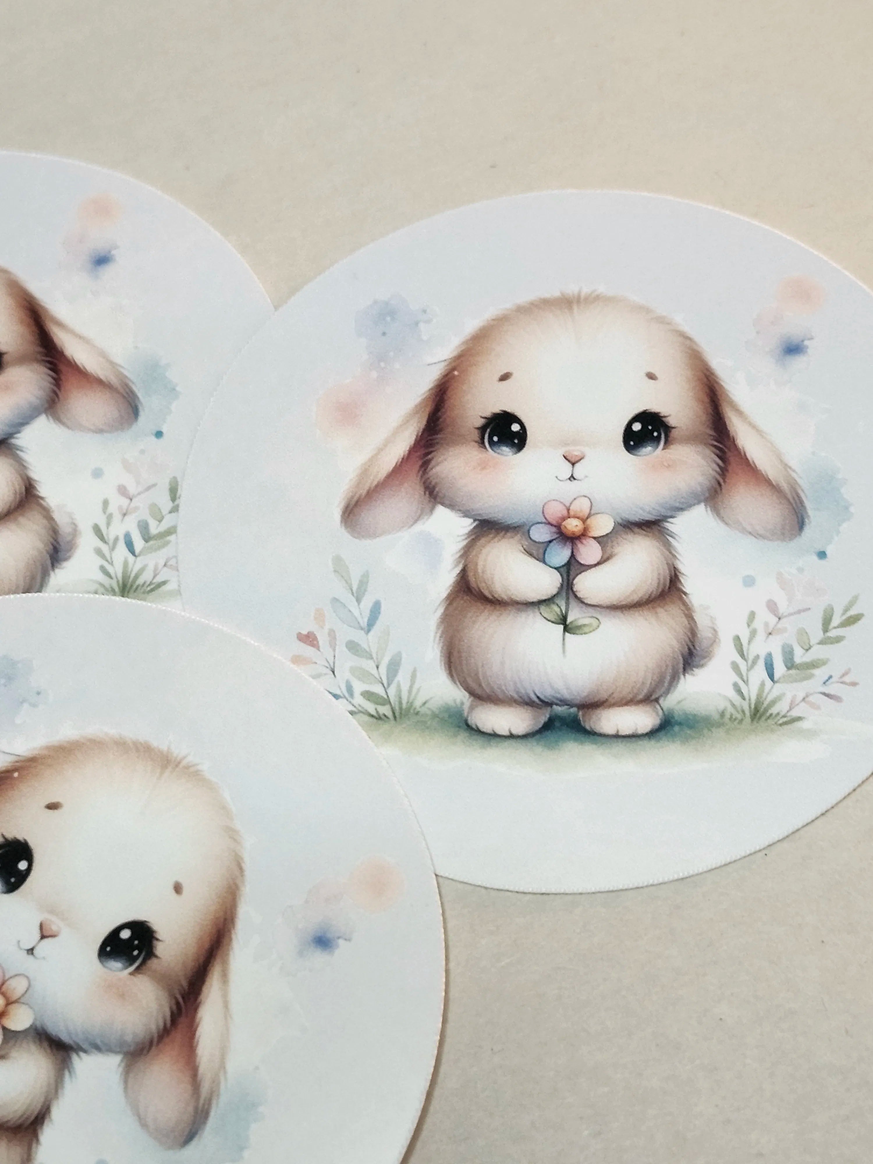 Three round stickers featuring cute cartoon bunny illustrations, arranged on a light beige surface.
