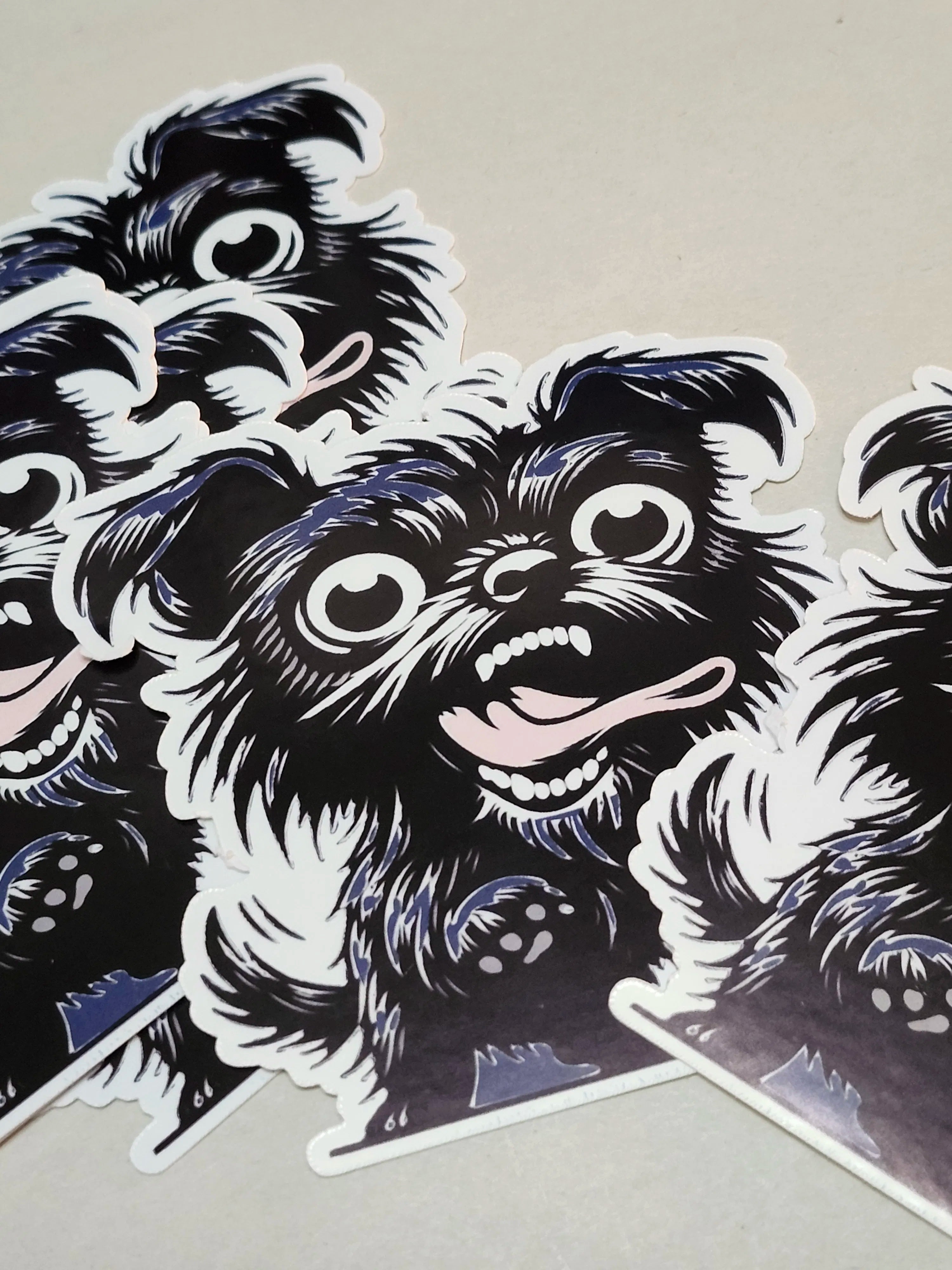 A close-up of several die-cut stickers featuring a stylized black and white cartoon dog face with blue-gray shading, arranged on a light neutral surface.