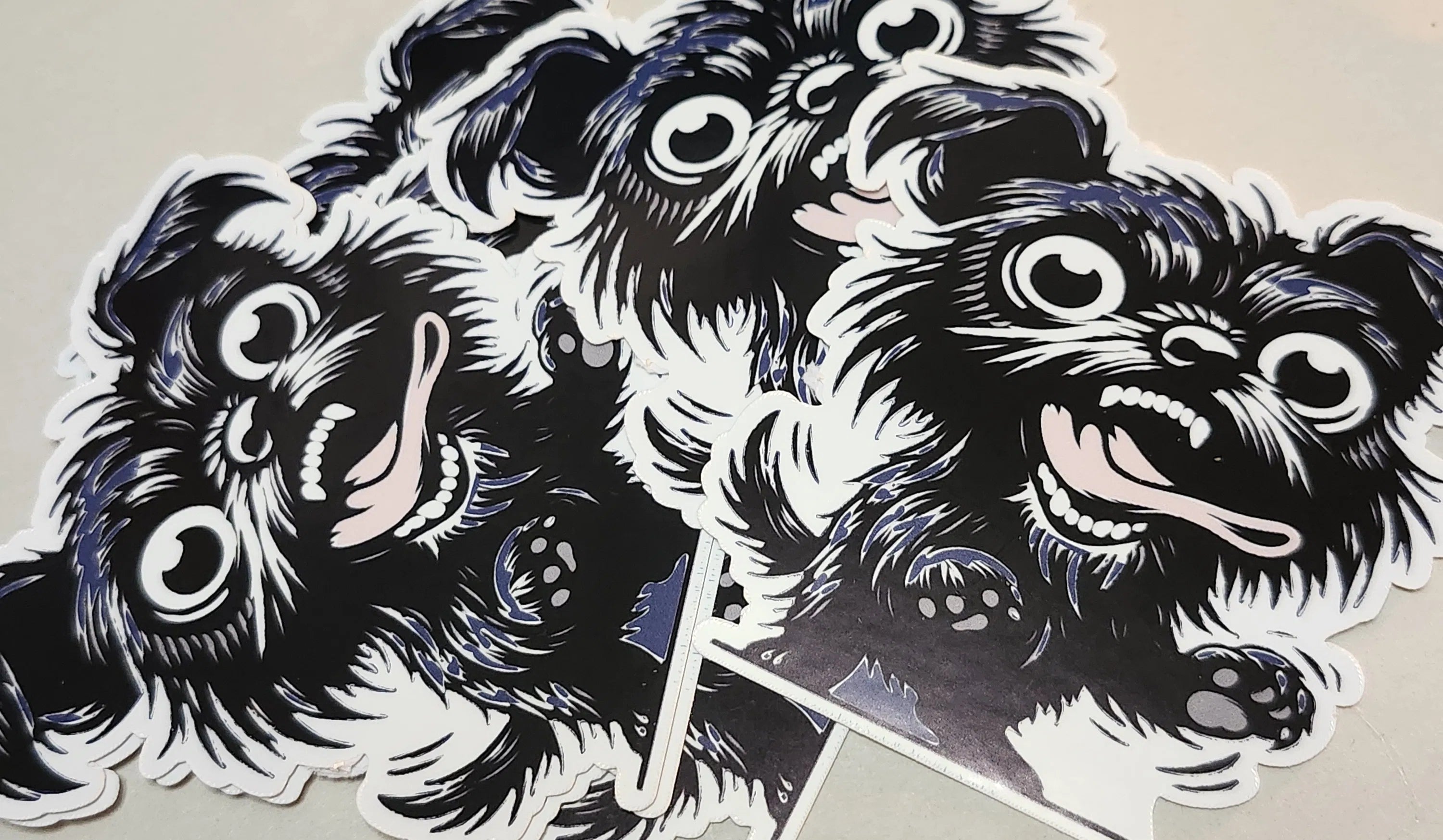 A close-up of several die-cut stickers featuring a black-and-white illustrated dog face with large eyes and an open mouth, arranged on a light beige surface.