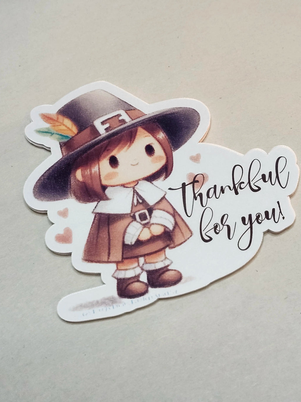 A die-cut sticker featuring a cute cartoon girl dressed as a Pilgrim with the text 'thankful for you!' on a light beige background.