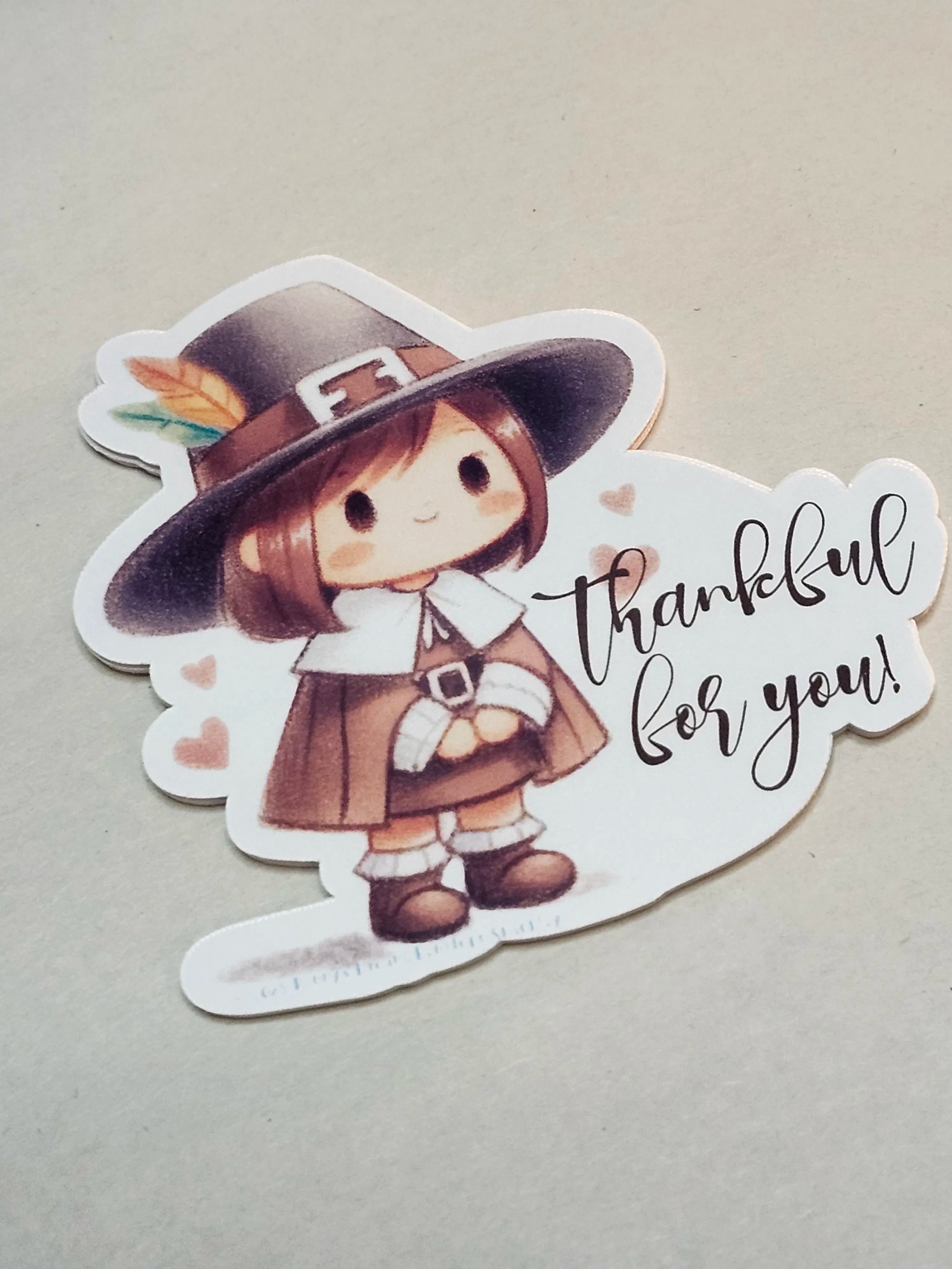 A die-cut sticker featuring a cute cartoon girl dressed as a Pilgrim with the text 'thankful for you!' on a light beige background.