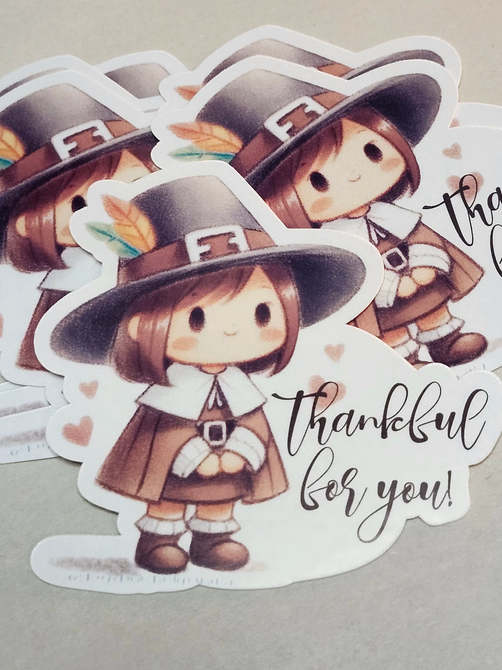 A stack of die-cut stickers featuring a cute cartoon Thanksgiving pilgrim girl in a brown hat and cloak with the text 'thankful for you!' on a light gray background.