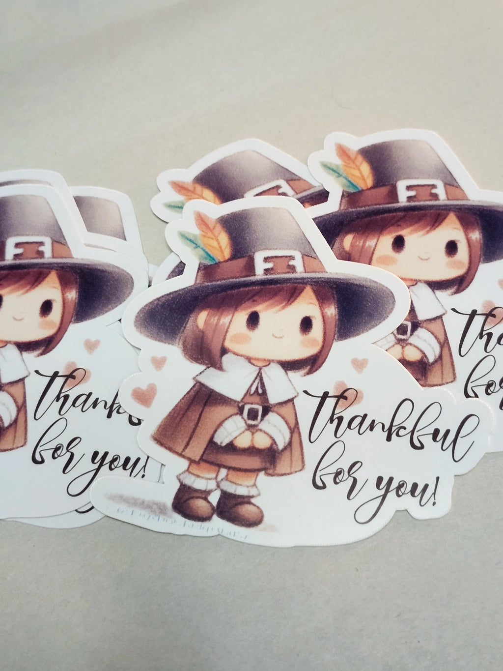 A set of die-cut stickers featuring a cute cartoon Thanksgiving pilgrim character wearing a brown hat with a feather, a brown outfit, and the phrase 'thankful for you!' in black script on a white background.