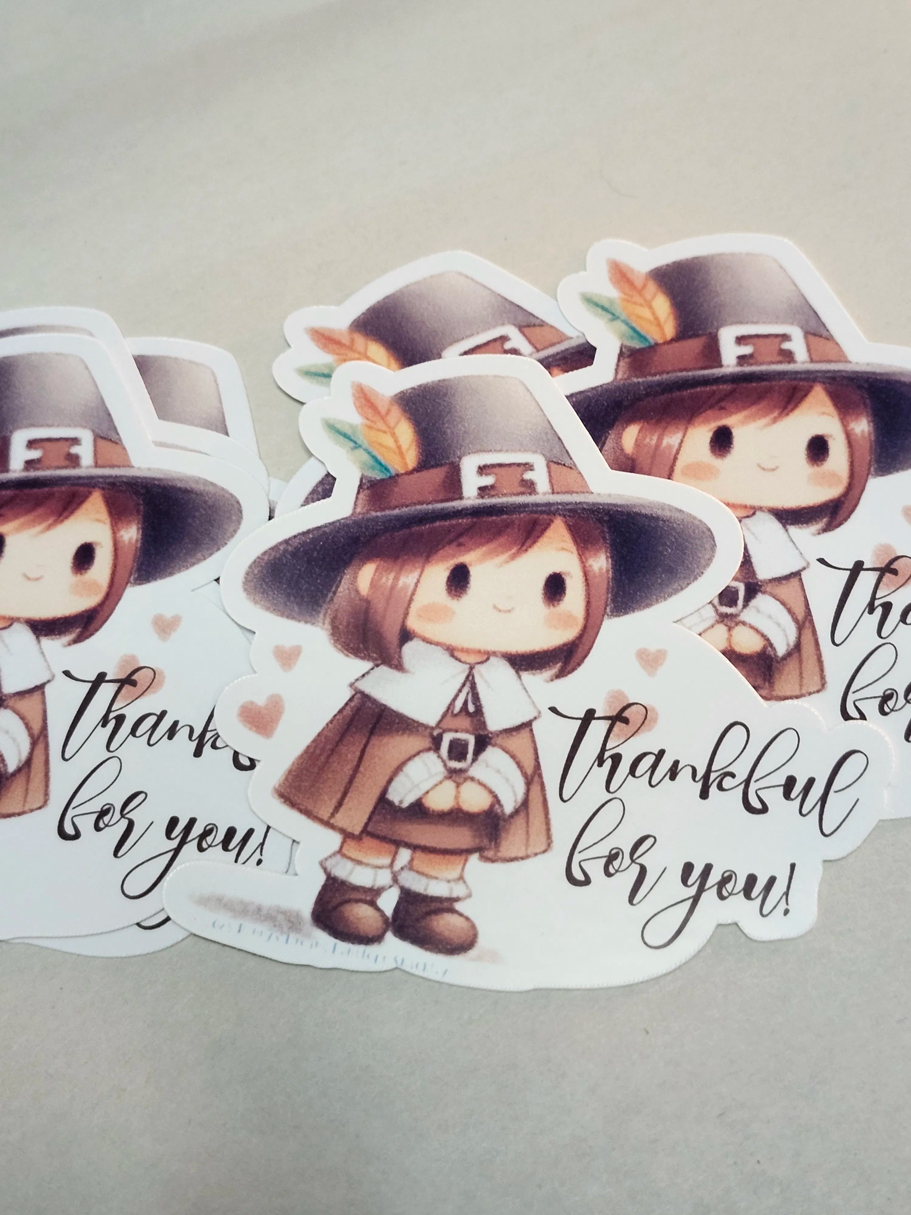 A set of die-cut stickers featuring a cute cartoon Thanksgiving pilgrim character wearing a brown hat with a feather, a brown outfit, and the phrase 'thankful for you!' in black script on a white background.
